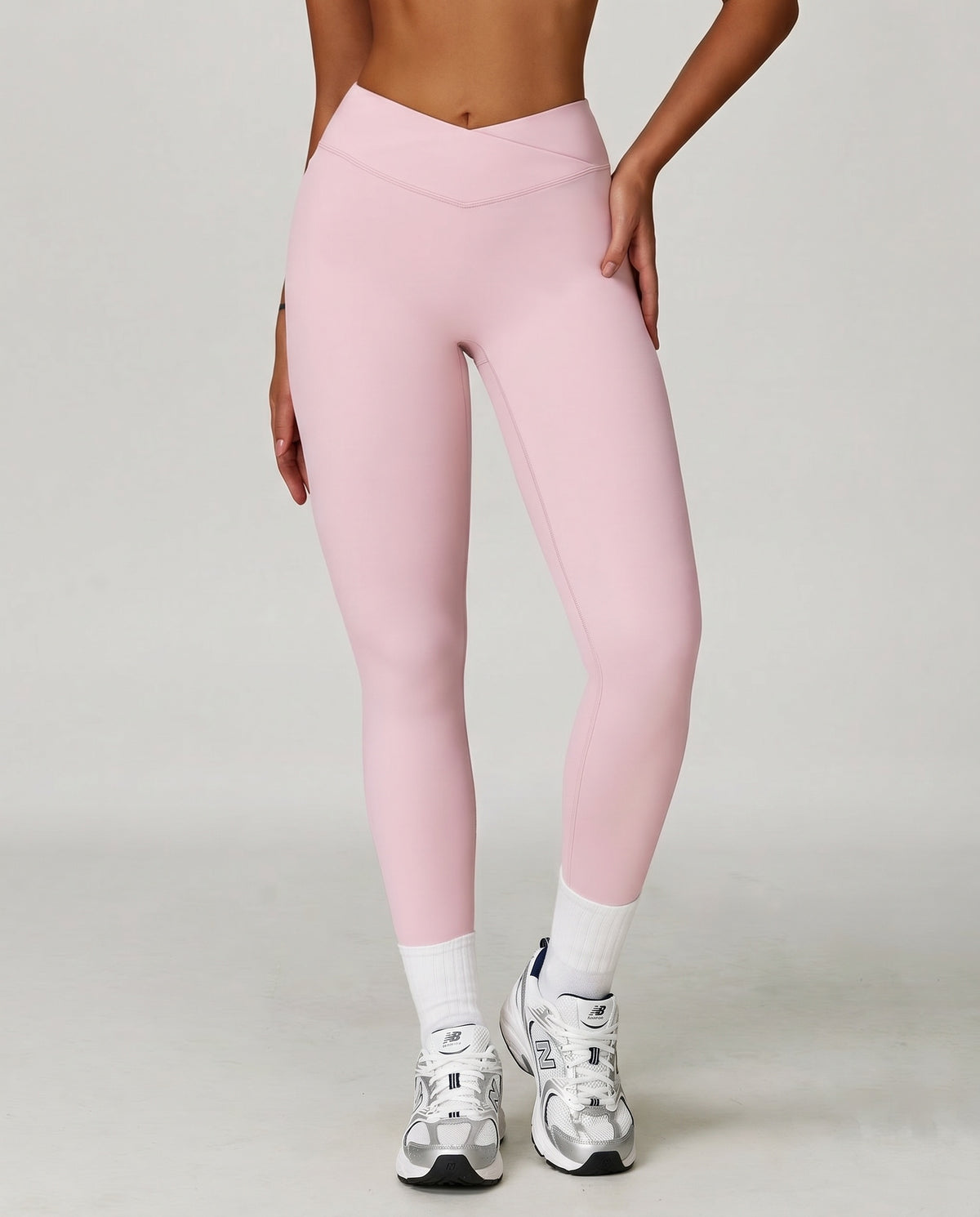Woman wearing pink high waist crossover compression leggings with V-shaped waistband, paired with white socks and sneakers, front view showing sculpting fit.