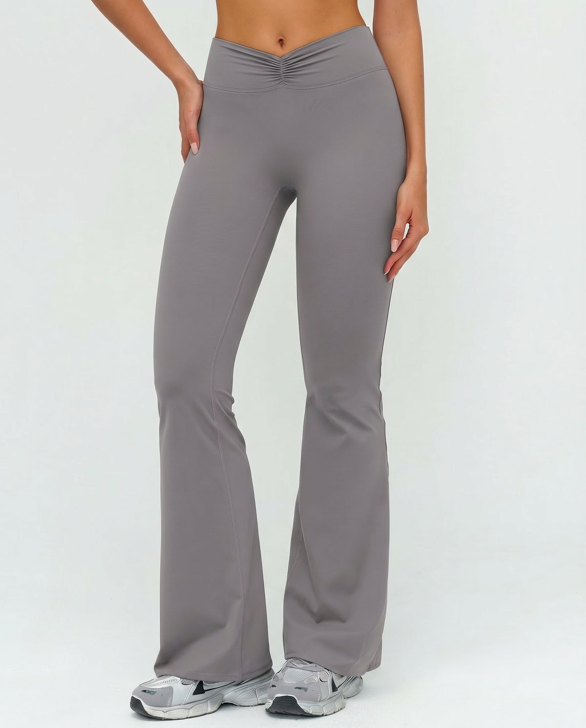 Front view of grey ruched high waist flare yoga leggings featuring a sculpting V-shaped waistband and flared leg silhouette, paired with grey sneakers.
