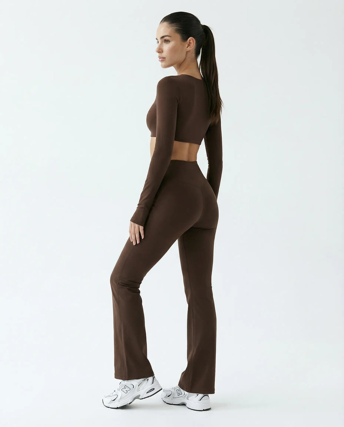 Woman wearing a fitted long sleeve crop top and high waist flare leggings activewear set styled with athletic sneakers.
