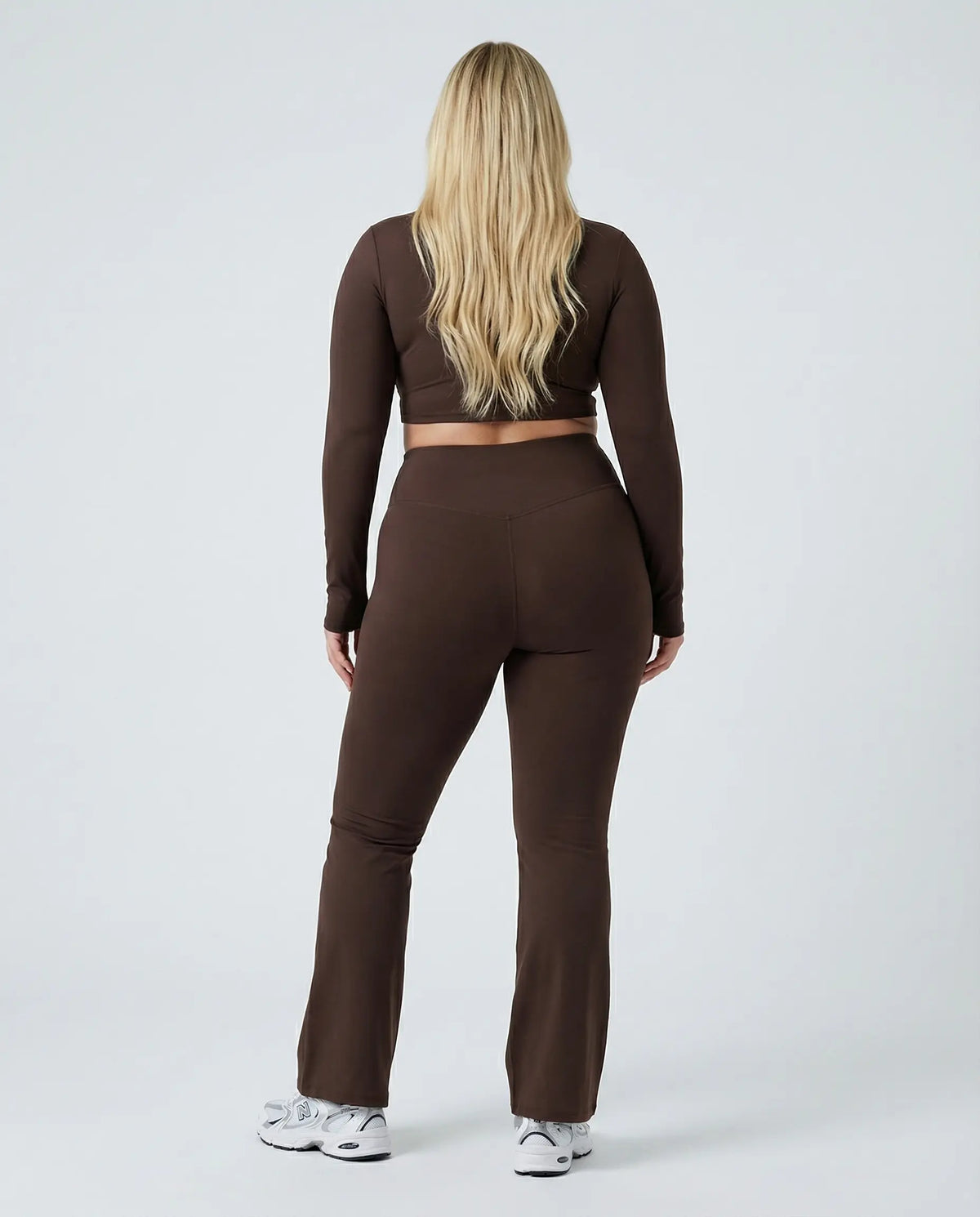 Woman wearing a fitted long sleeve crop top and high waist flare leggings activewear set styled with athletic sneakers.