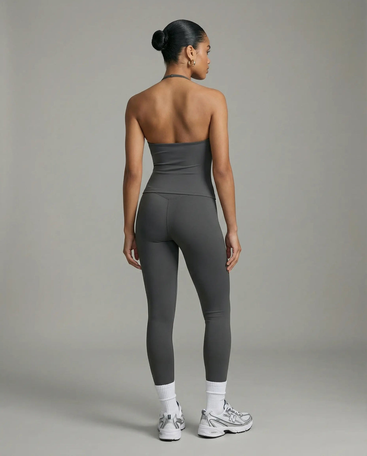 Model wearing a gray seamless halter sculpt leggings set with high waist fitted leggings and athletic sneakers.