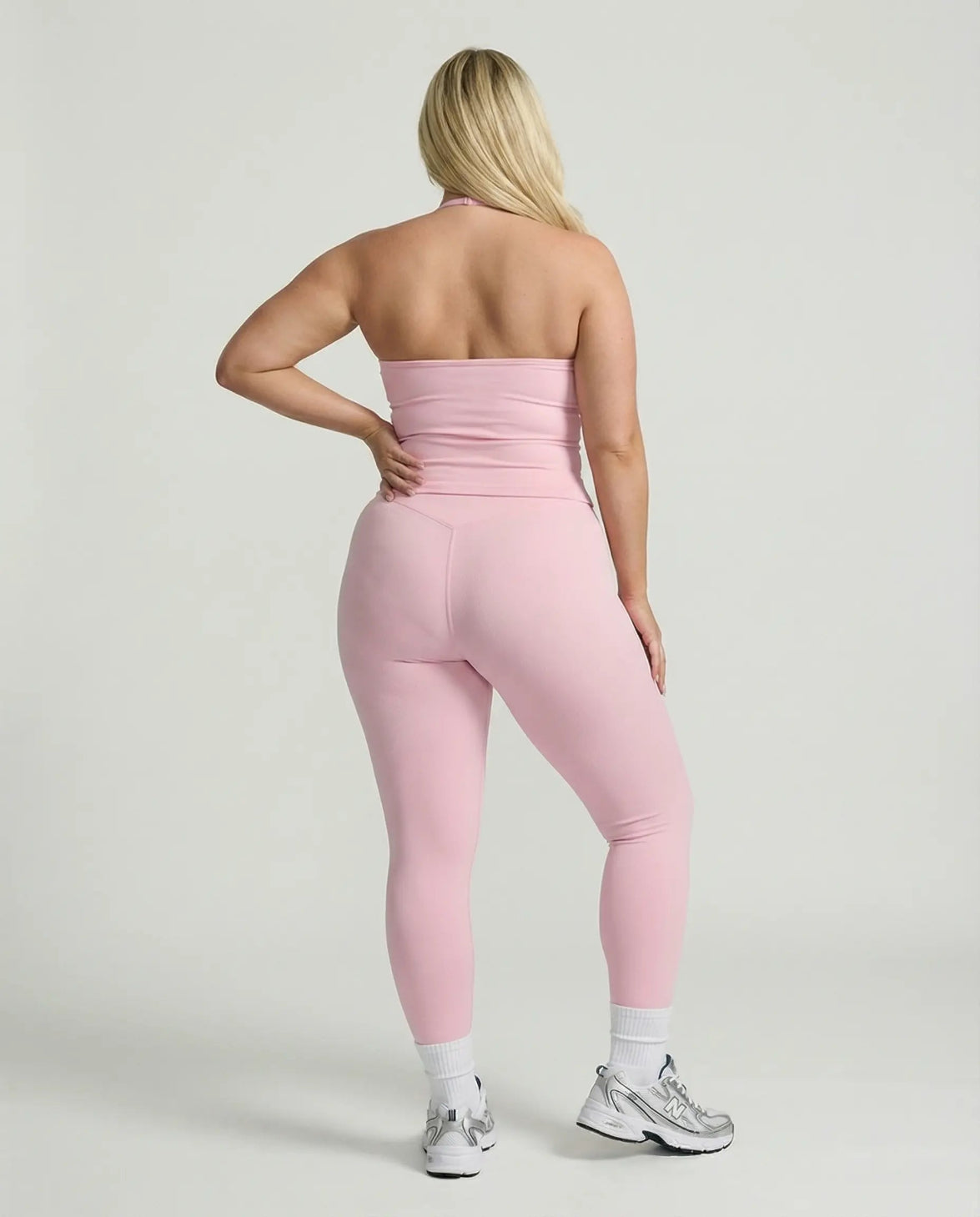 Model wearing a pink seamless halter sculpt leggings set with high waist fitted leggings and athletic sneakers.