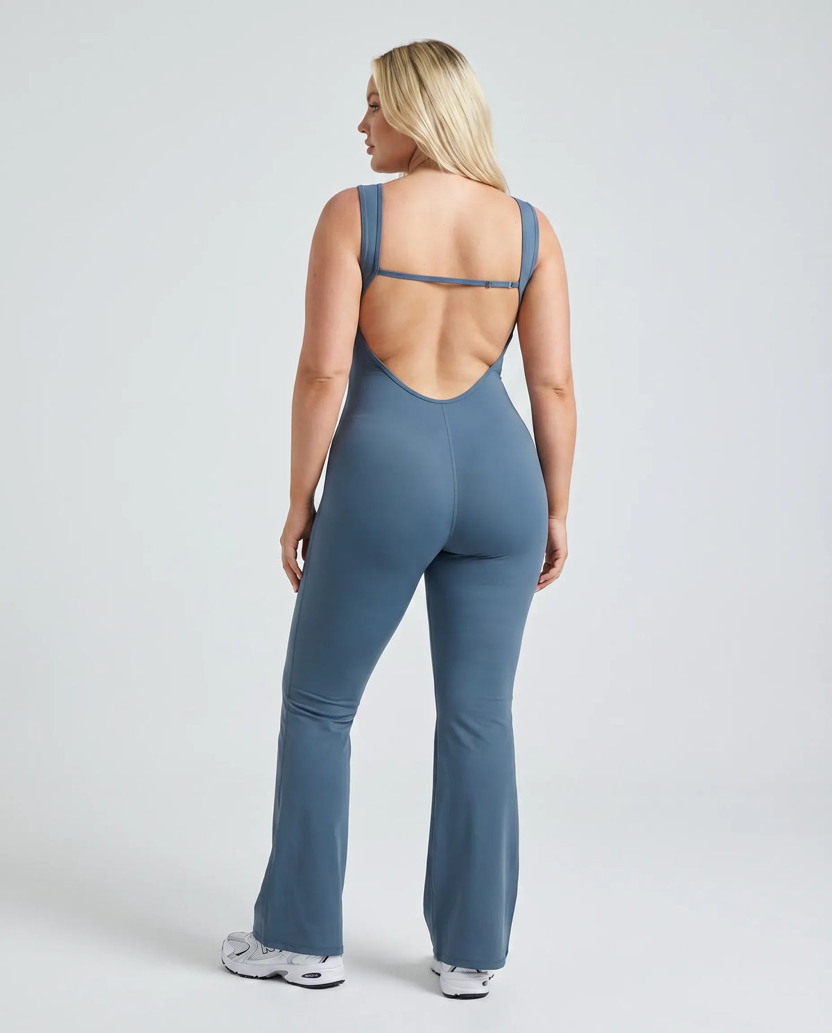Model facing away showing the open back design of the blue backless flare bodysuit in studio lighting.