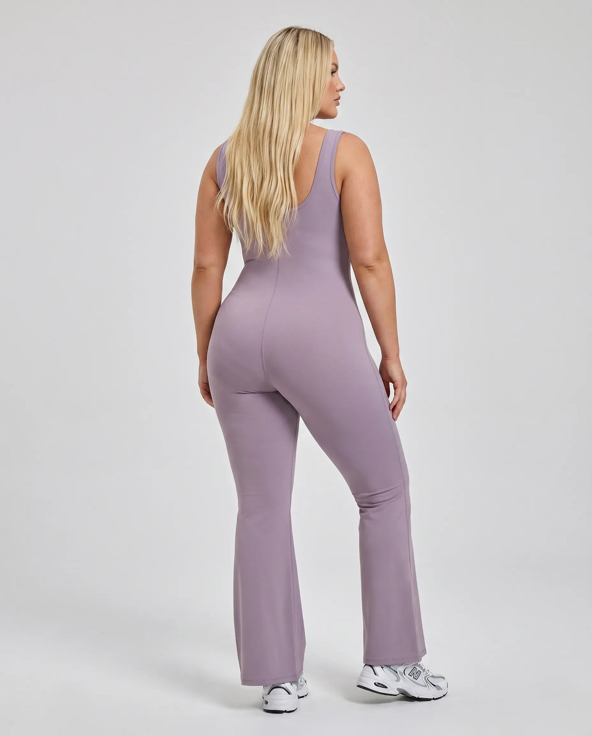 Model facing away in studio showing the open back detail of the purple sculpting bodysuit.