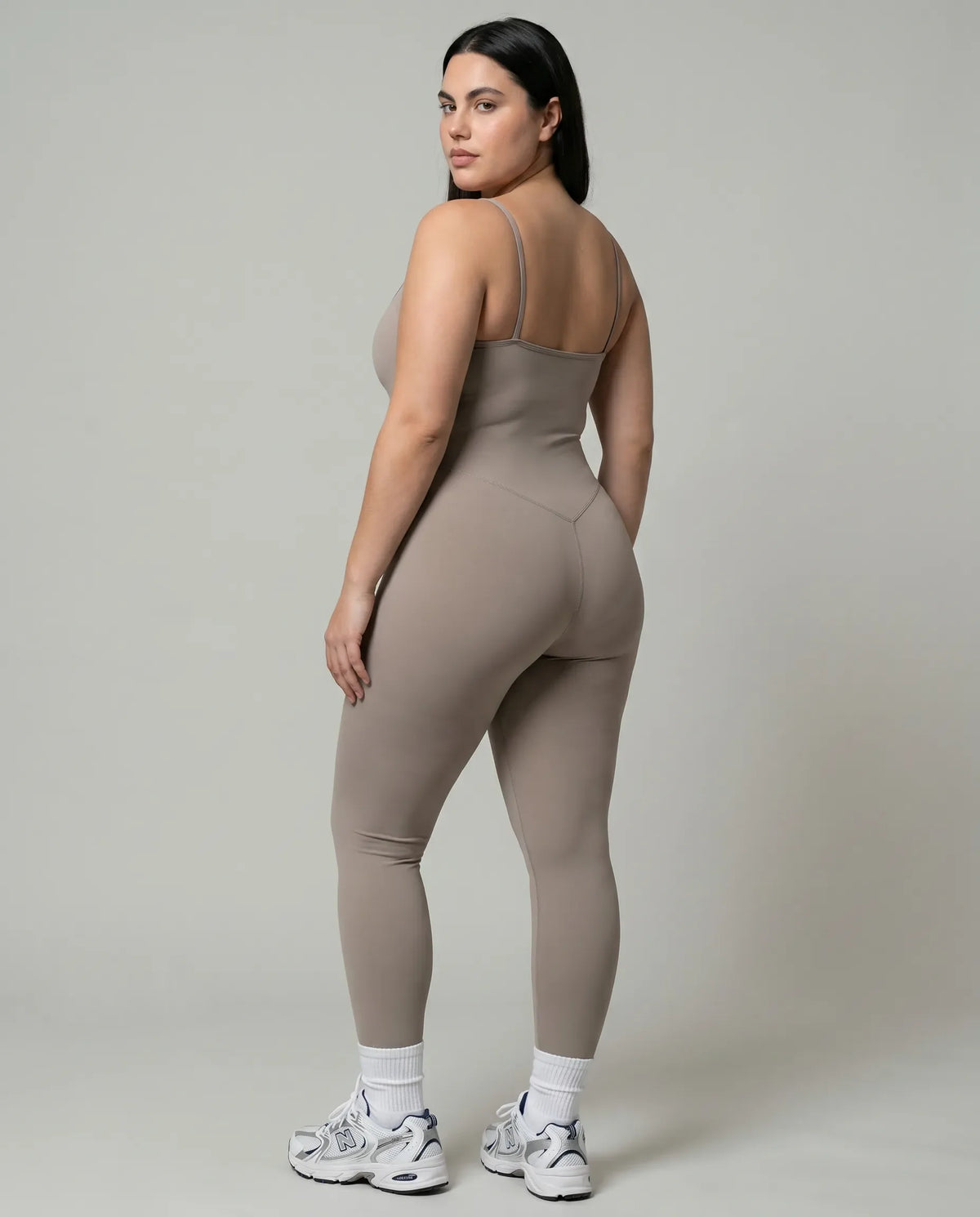 Model wearing gray backless bodysuit from behind in studio showing open back detail and full-length leg.