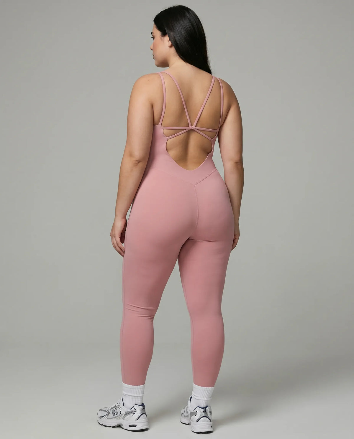Female model rear studio shot showing the open back design of the pink full-length bodysuit.