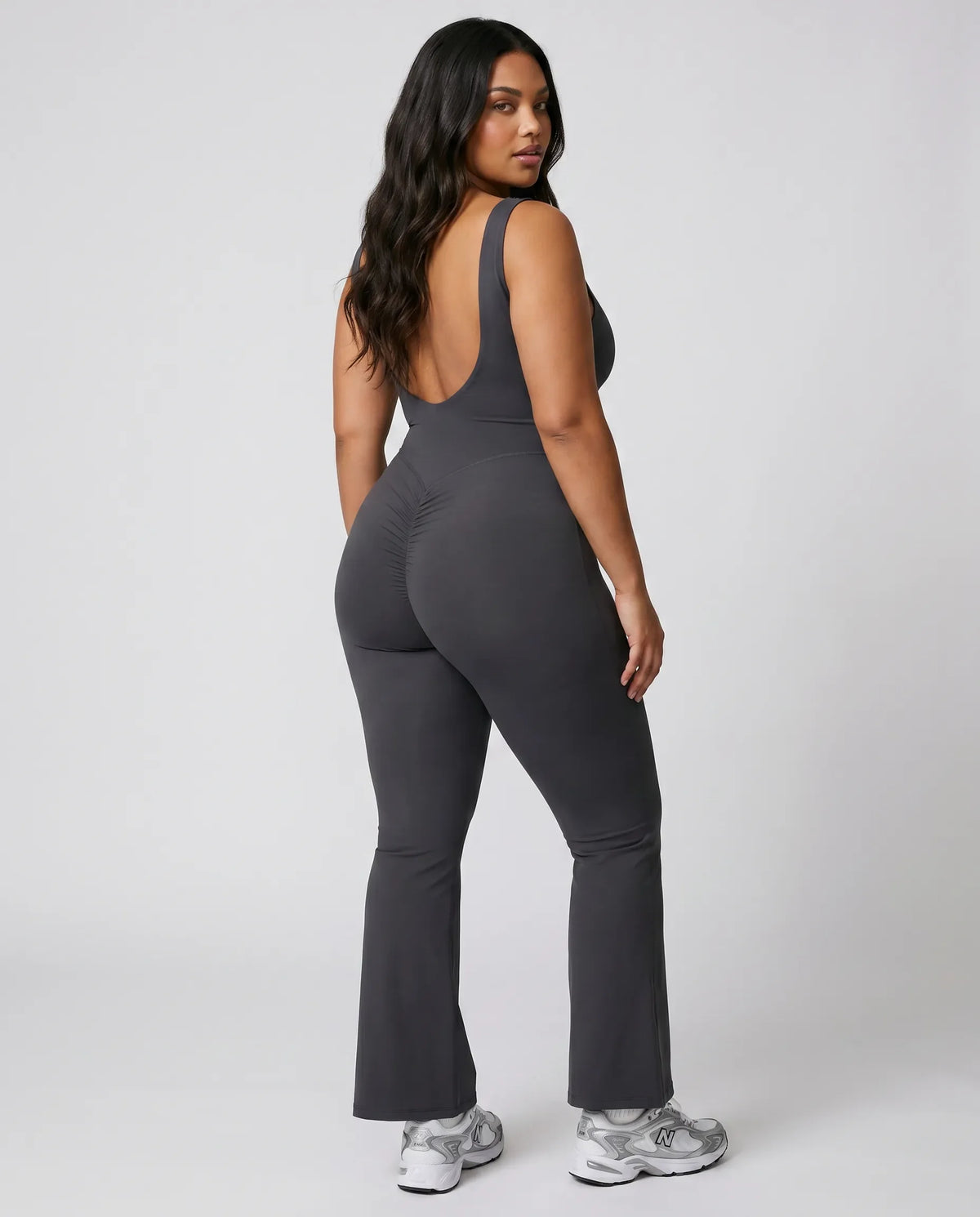 Model facing away from camera showing the deep open back of the ash bodysuit in a studio setting.