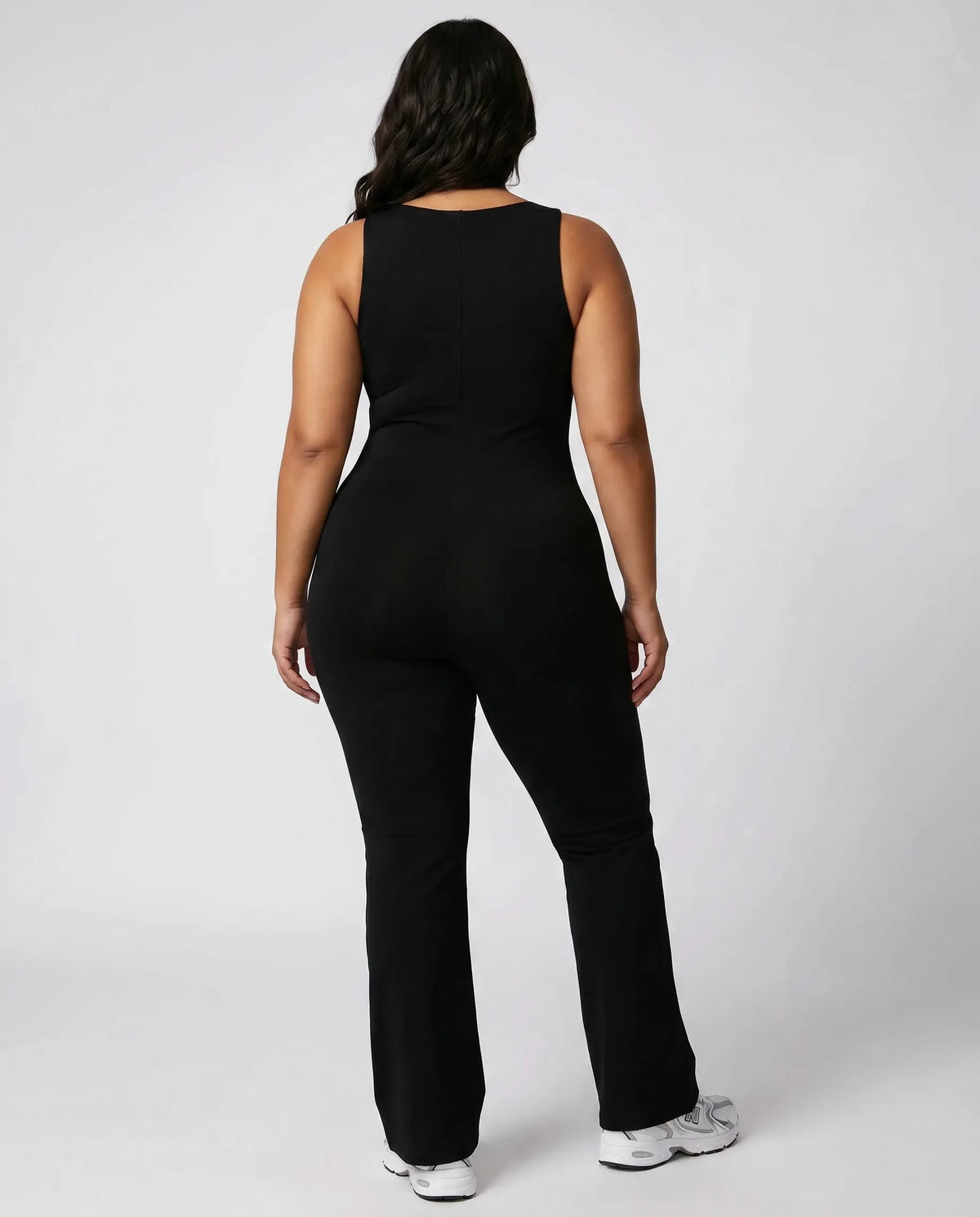 Model wearing black backless flare bodysuit from behind showing the open back and clean seam lines.