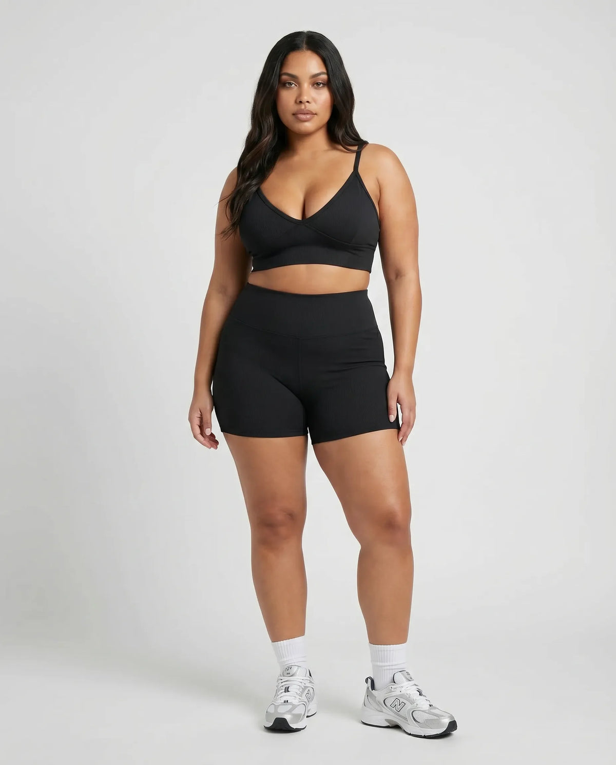 Model standing front-on in a studio wearing a black sculpting bra top paired with black bike shorts and sneakers.