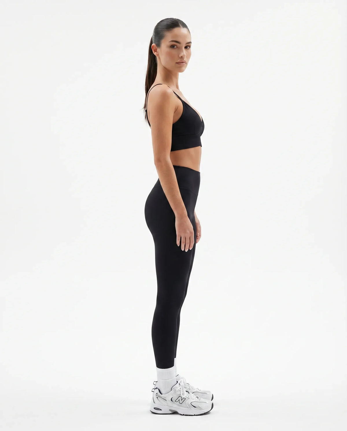Plus size model facing front in a studio wearing a black compression bra top with a sculpting V-neckline.