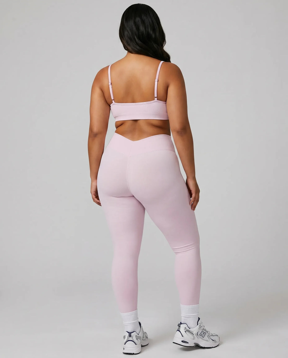 Model wearing pink ribbed bra top and matching leggings, rear studio view showing back coverage and strap placement.