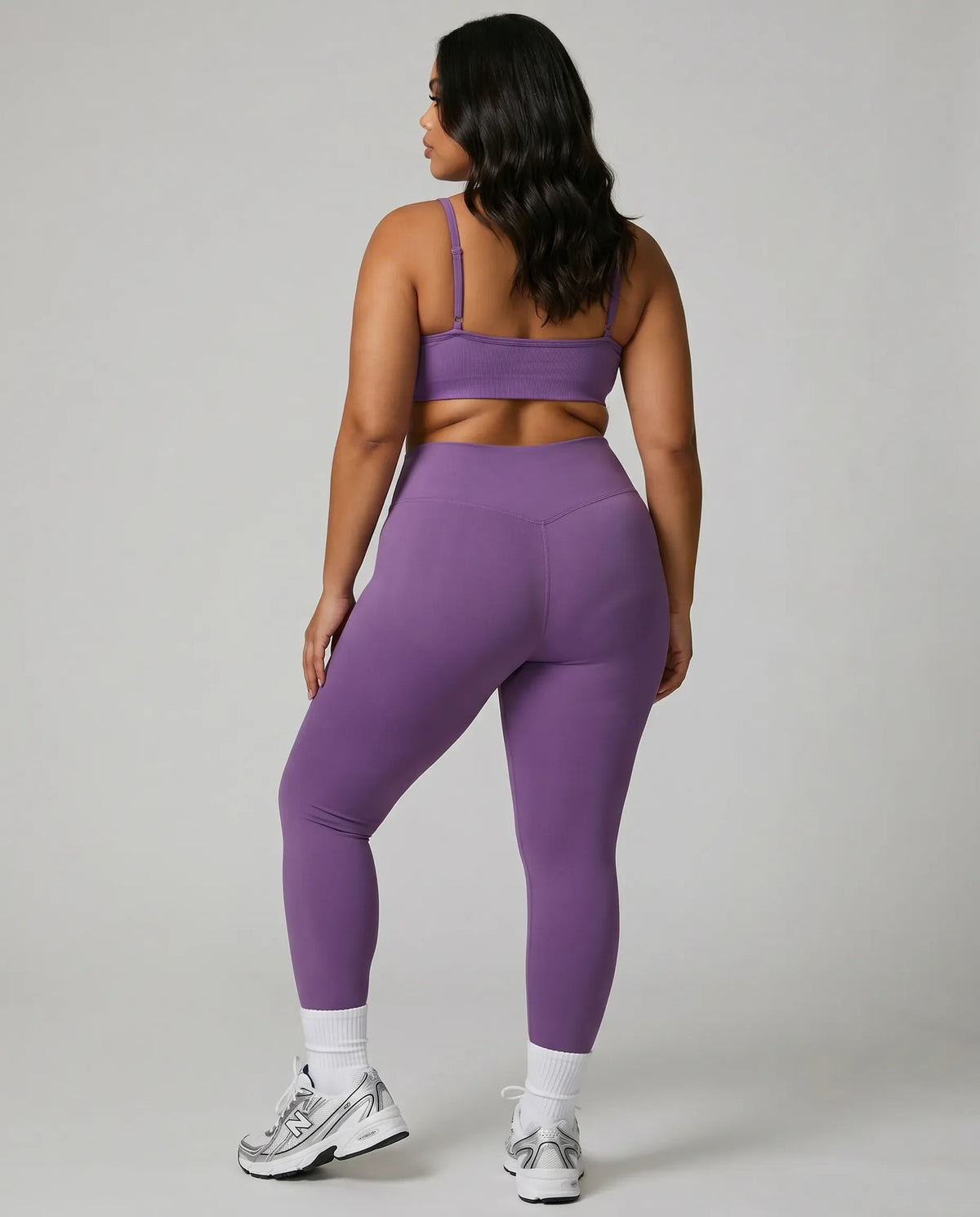 Model facing away in studio showing the back fit of the purple seamless bra top and high waist legging set.