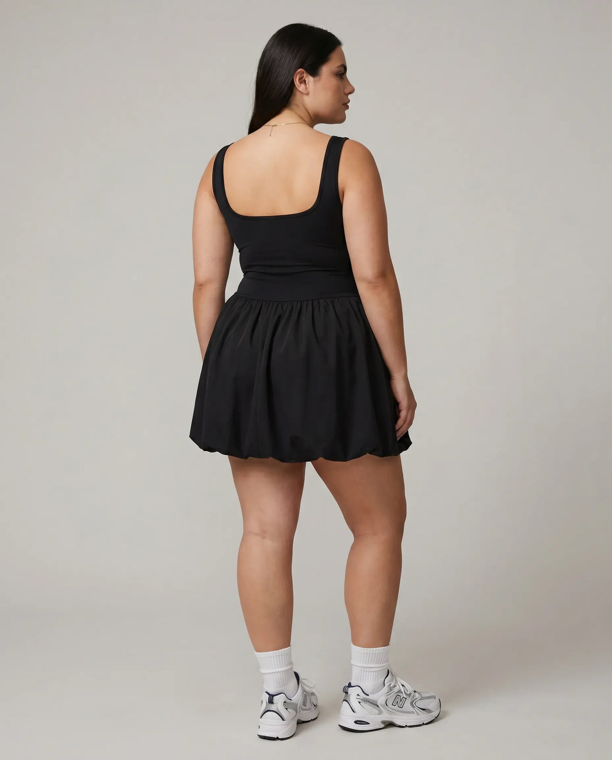 Model facing away showing the back of the black balloon mini dress in a studio setting.
