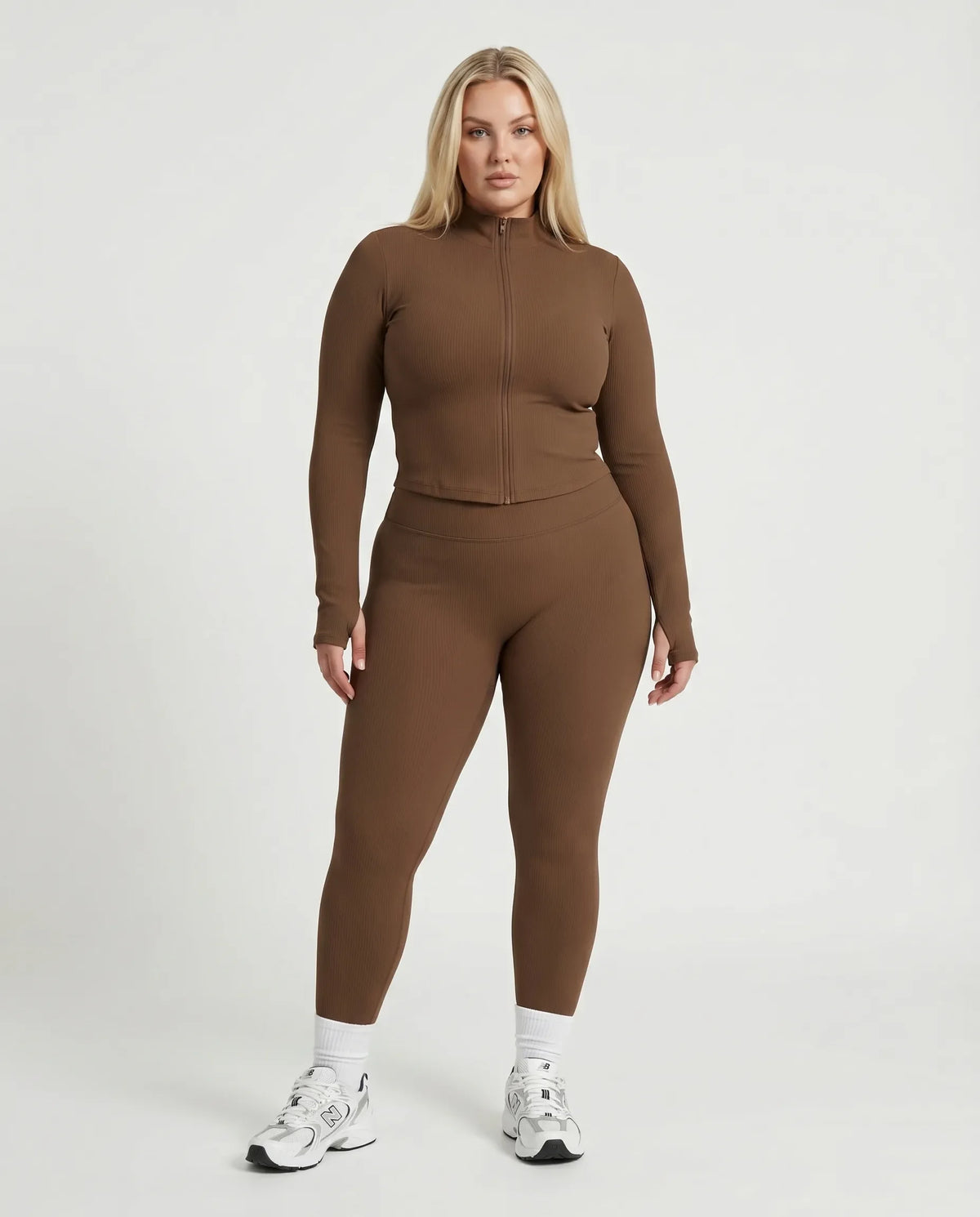 Female model facing forward in studio wearing brown ribbed sculpting zip jacket paired with matching brown leggings.