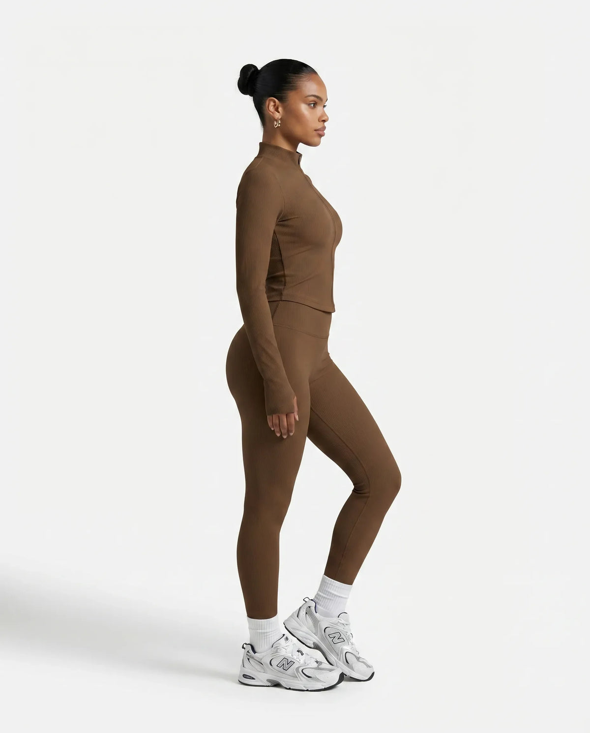 Lifestyle shot of woman wearing brown ribbed zip jacket outdoors walking with confidence in an athleisure setting.