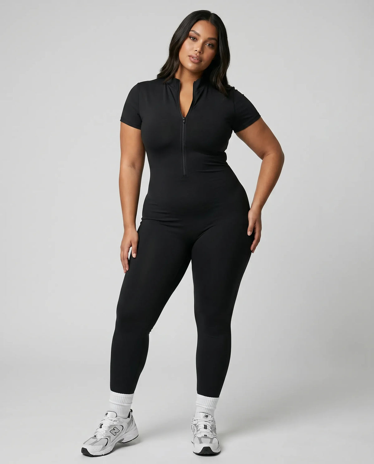 Model standing front-on in studio wearing brown sculpting jumpsuit legging with short sleeves and front zip closure.