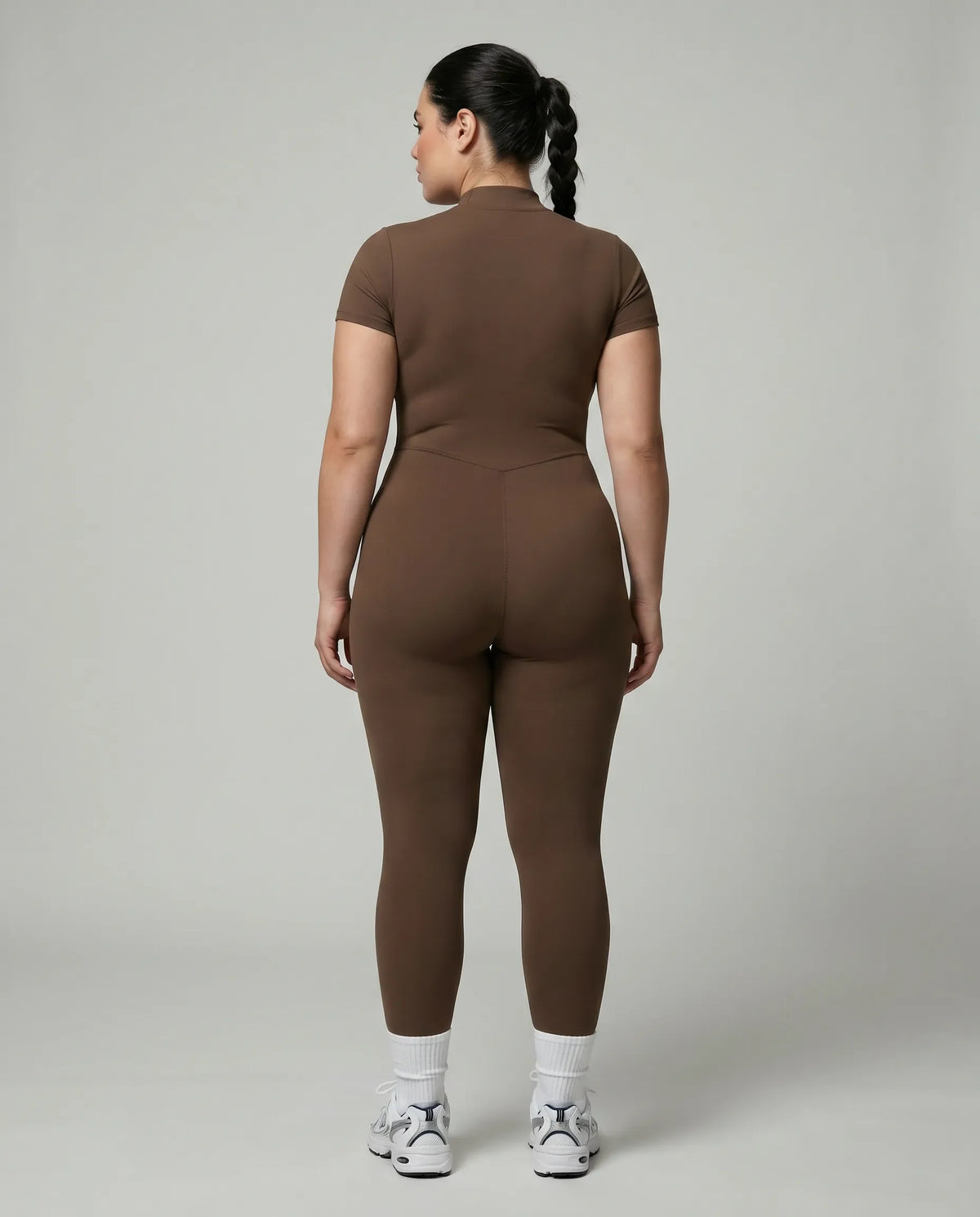Female model rear studio view wearing black full-length activewear jumpsuit showing back silhouette and seamless construction.