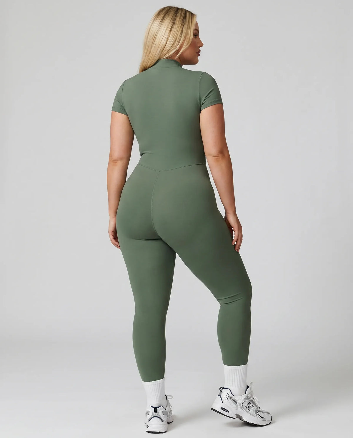 Female model from behind wearing green ribbed half-zip jumpsuit showing back fit in studio setting.