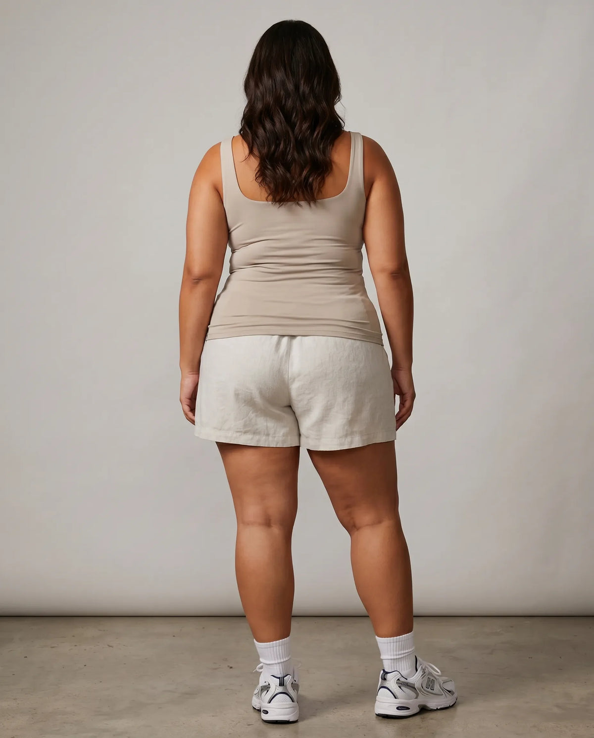 Model wearing beige sleeveless tank top photographed from behind in studio lighting.