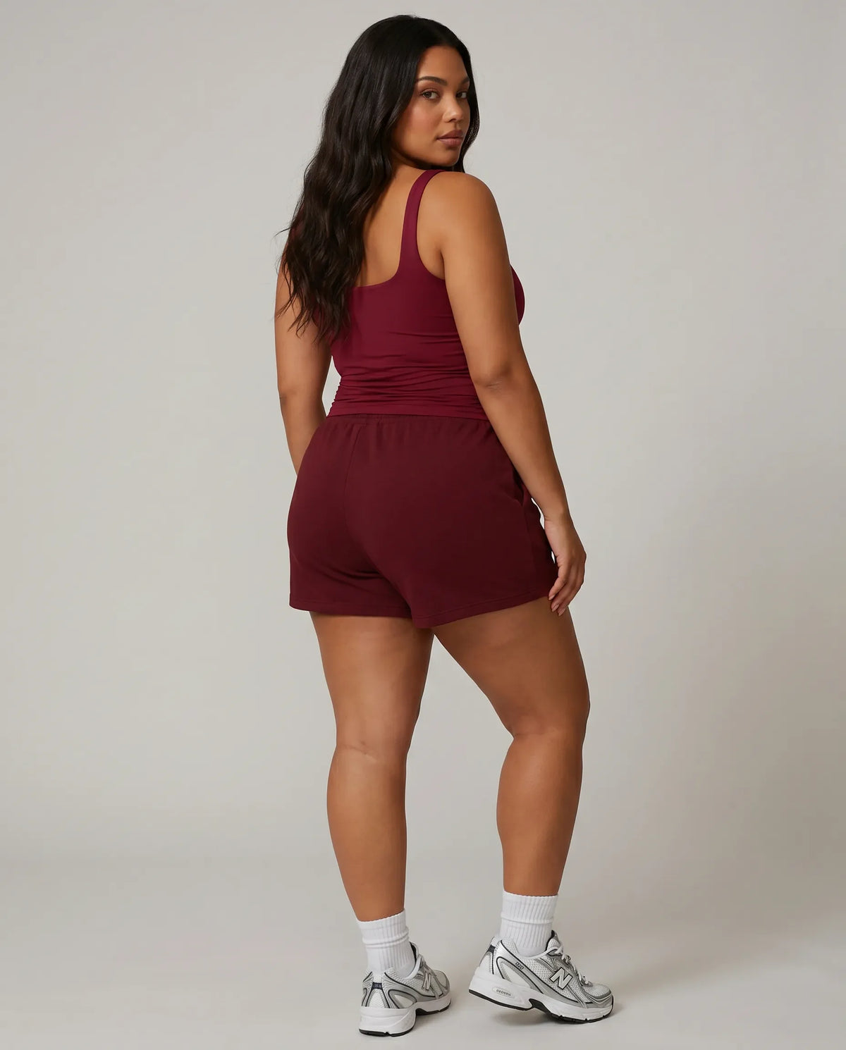Female model standing with back to camera in studio wearing red sleeveless tank top showing back fit and strap detail.