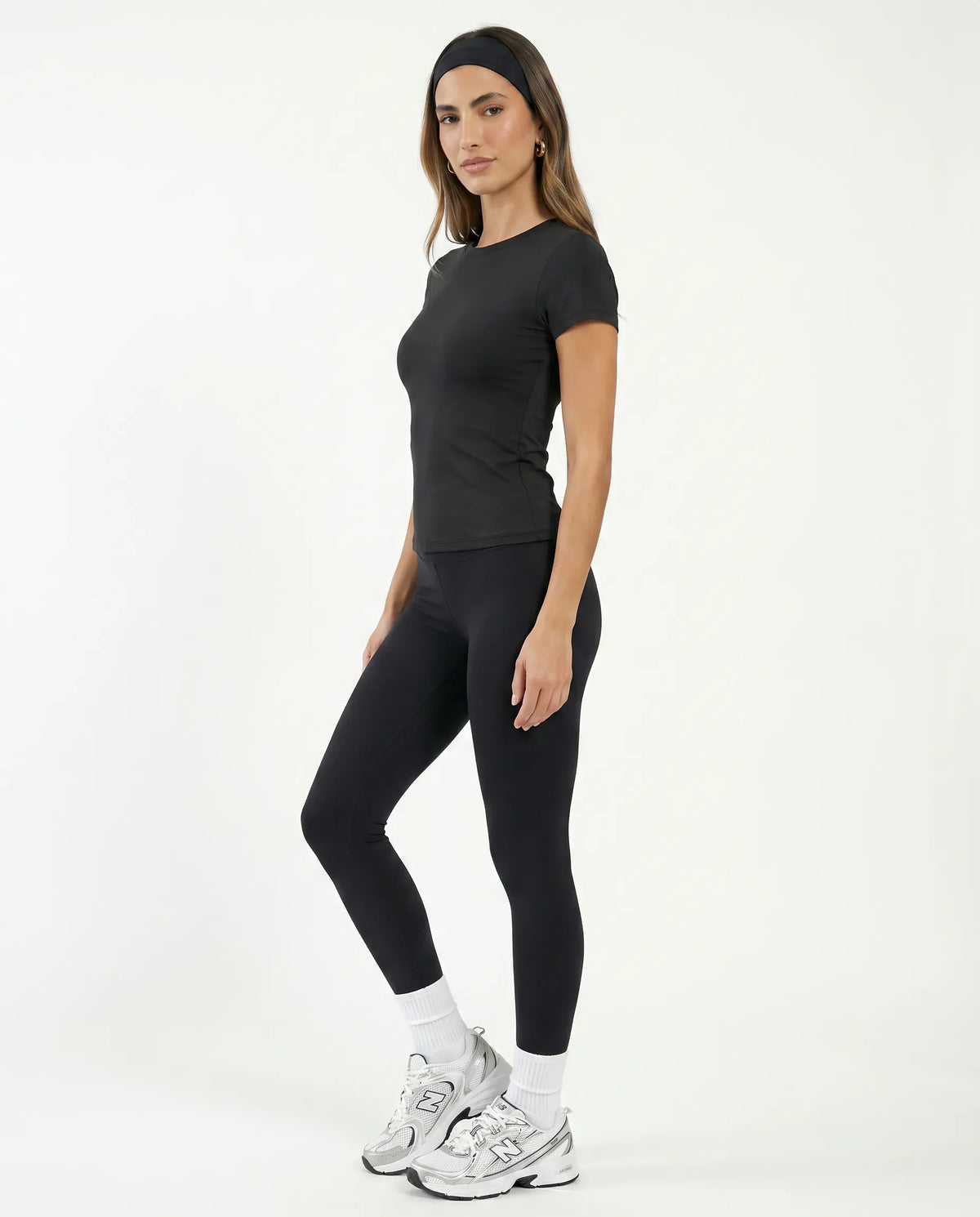 Lifestyle shot of a woman in the black crew neck t-shirt top walking outdoors with coffee, styled with bike shorts and sneakers.