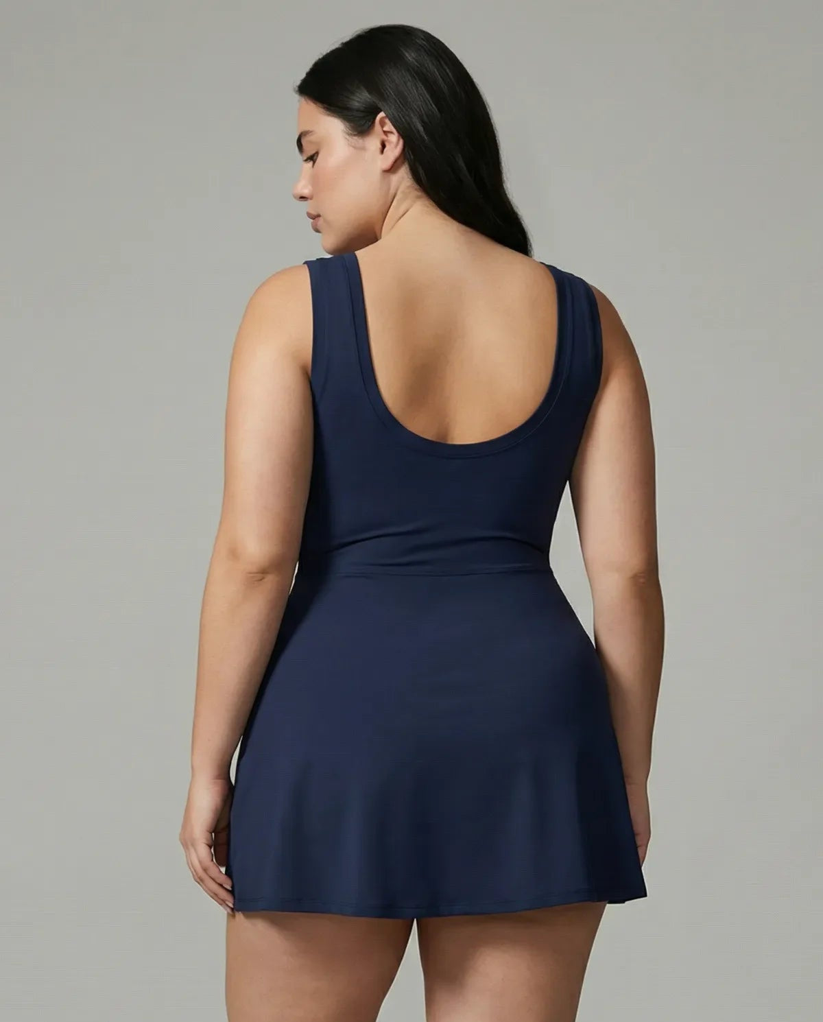 Model wearing blue active dress with wrap skirt tie detail, back view in studio showcasing the fitted bodice and skirt drape.