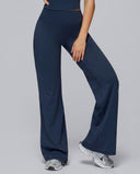Woman wearing navy flare high waist sculpting yoga leggings with a wide flare leg and compression waistband, paired with white sneakers against a grey background.