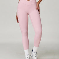 Woman wearing pink high waist crossover compression leggings with V-shaped waistband, paired with white socks and sneakers, front view showing sculpting fit.