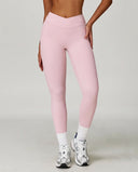 Woman wearing pink high waist crossover compression leggings with V-shaped waistband, paired with white socks and sneakers, front view showing sculpting fit.