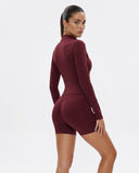 Woman wearing a fitted Burgundy activewear set with high waist shorts and a zip-up jacket in a clean studio setting.