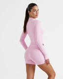 Woman wearing a fitted activewear set with sculpting high waist shorts and a long sleeve zip jacket in a soft pink tone.