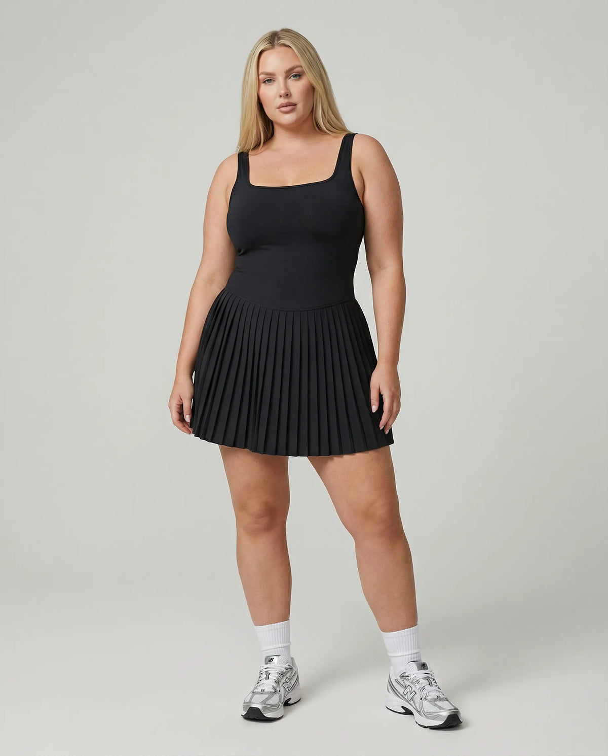 Women's black tennis dress with pleated skirt and square neckline displayed on ghost mannequin, front view.