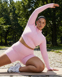 Woman wearing a fitted activewear set with sculpting high waist shorts and a long sleeve zip jacket in a soft pink tone.
