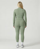 Woman wearing a seamless sculpting three piece activewear set with high waist leggings, sports bra, and fitted jacket paired with sneakers.