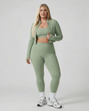 Woman wearing a seamless sculpting three piece activewear set with high waist leggings, sports bra, and fitted jacket paired with sneakers.