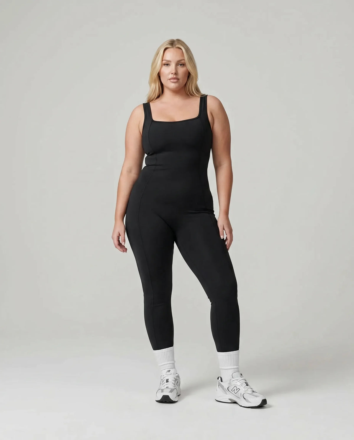 Model standing front-on in the black backless bodysuit in a white studio, showing the sculpting torso fit.