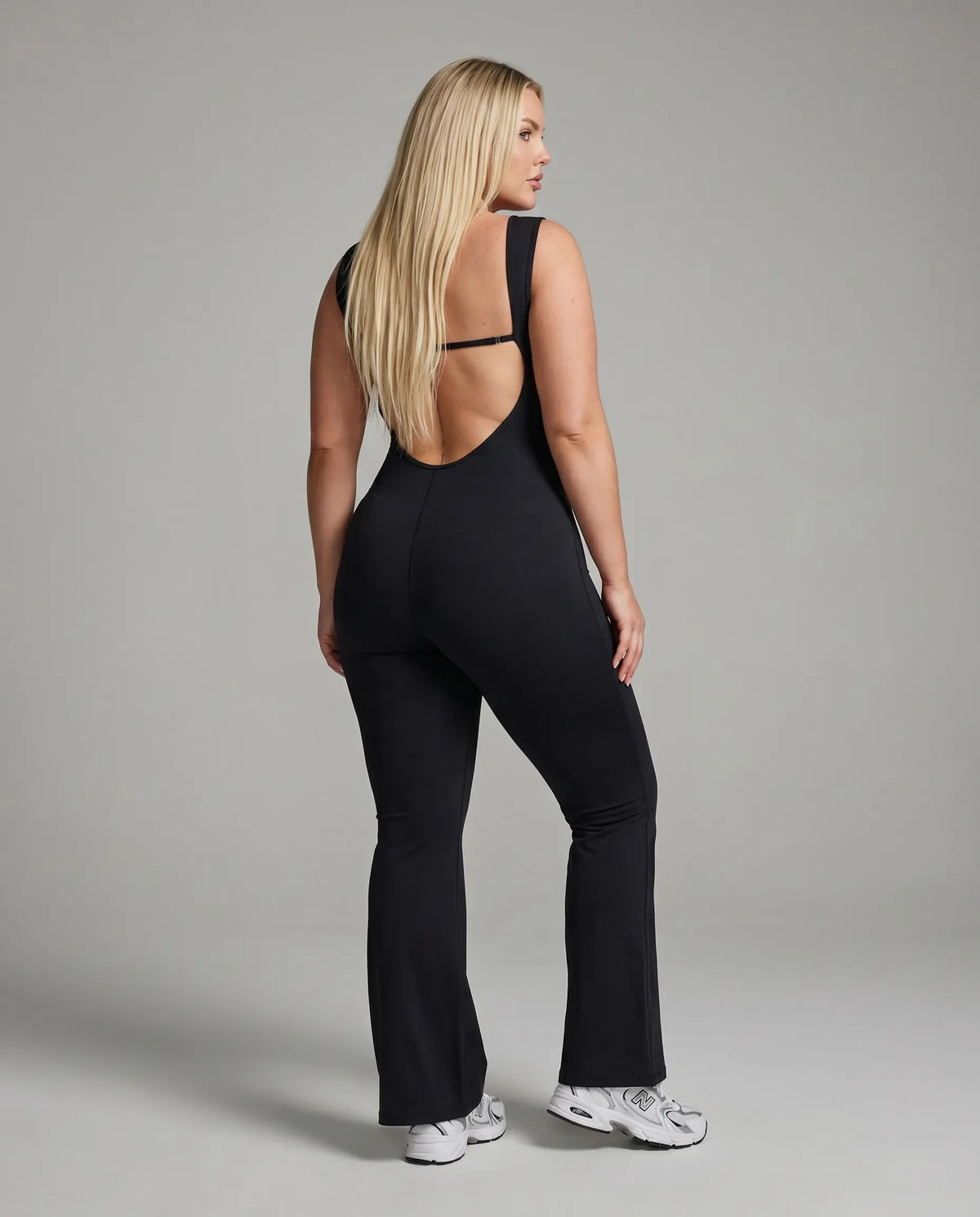 Model facing away in the black backless bodysuit, displaying the full open back design in studio lighting.