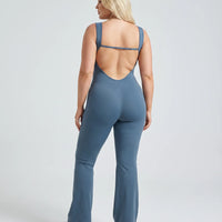 Model facing away showing the open back design of the blue backless flare bodysuit in studio lighting.