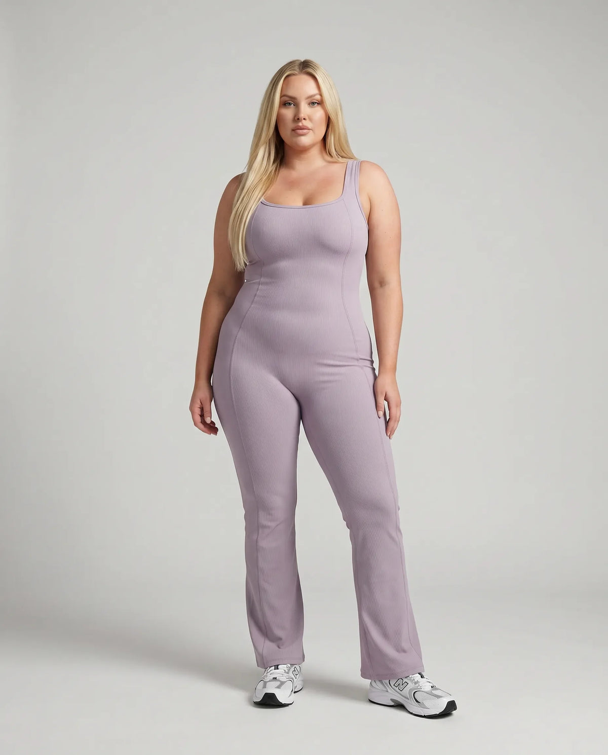 Model standing front-on in studio wearing purple flared leg backless bodysuit with white sneakers.