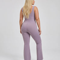 Model facing away in studio showing the open back detail of the purple sculpting bodysuit.