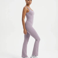 Plus size model front view wearing purple backless bodysuit with flared legs in studio setting.