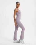Plus size model front view wearing purple backless bodysuit with flared legs in studio setting.