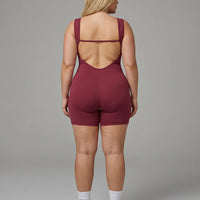 Female model wearing red backless sculpting bodysuit, rear view showing open back detail in studio.