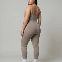 Model wearing gray backless bodysuit from behind in studio showing open back detail and full-length leg.