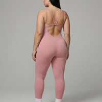 Female model rear studio shot showing the open back design of the pink full-length bodysuit.