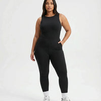Model wearing black backless flare bodysuit standing front-on in a white studio with hands relaxed.