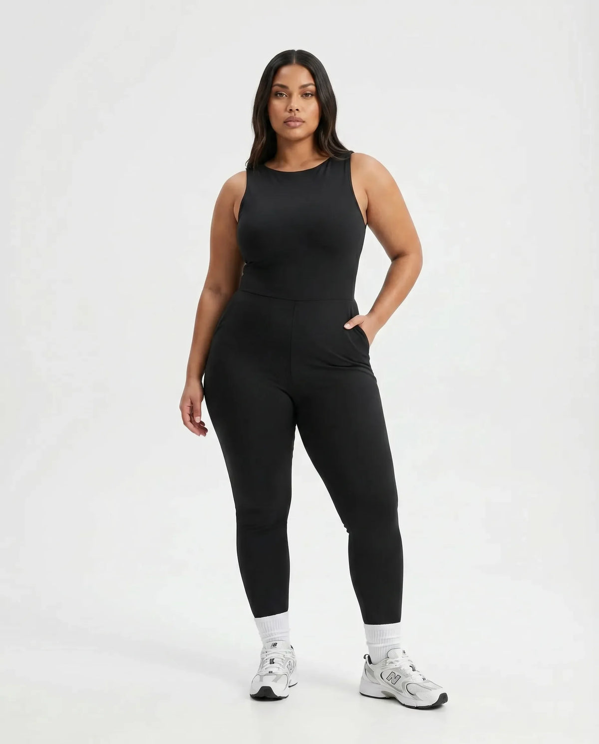 Model wearing black backless flare bodysuit standing front-on in a white studio with hands relaxed.