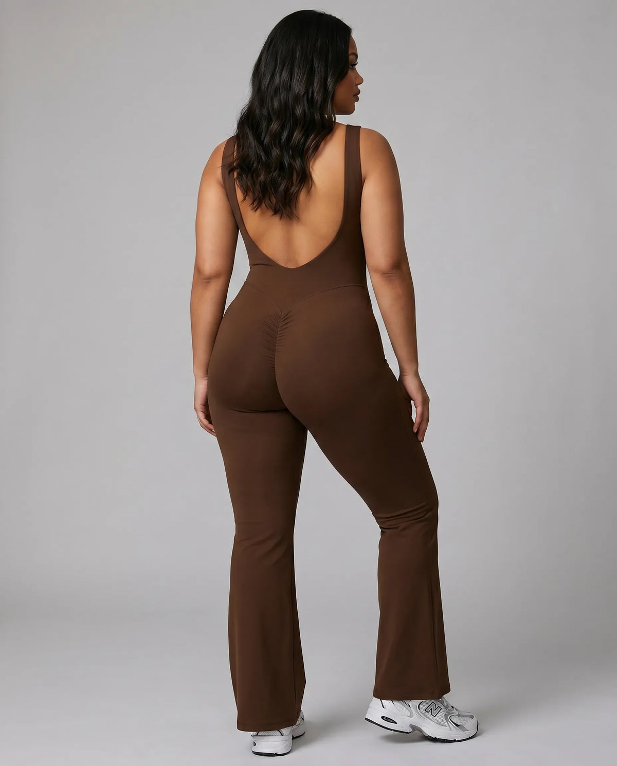 Model shown from behind wearing brown backless flare bodysuit, displaying the open back detail in studio lighting.
