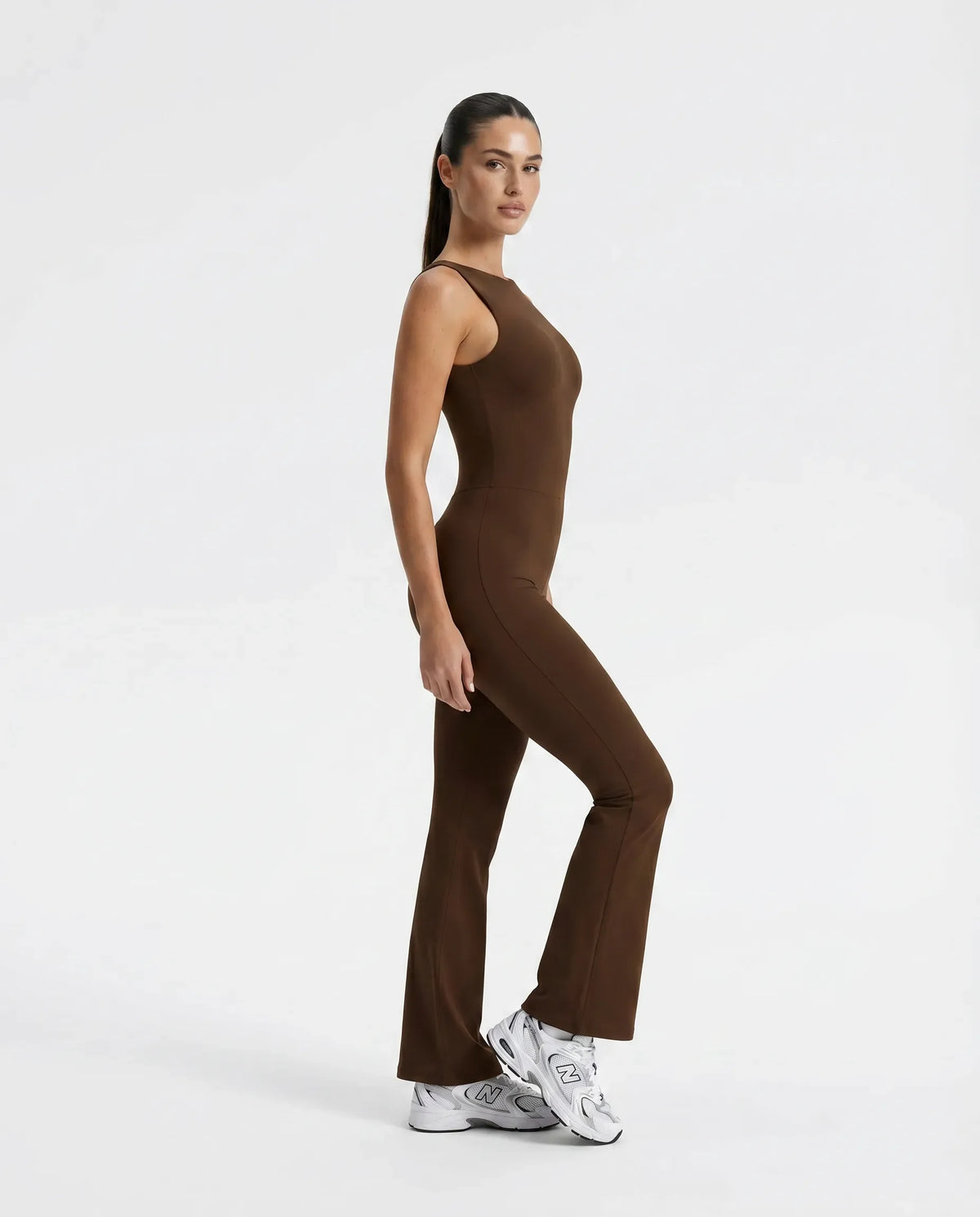Plus size model facing forward wearing brown backless flare bodysuit, showing sculpting fit across the torso and flared legs.