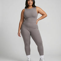 Model standing front-on in a studio wearing the purple backless flare bodysuit with white sneakers.